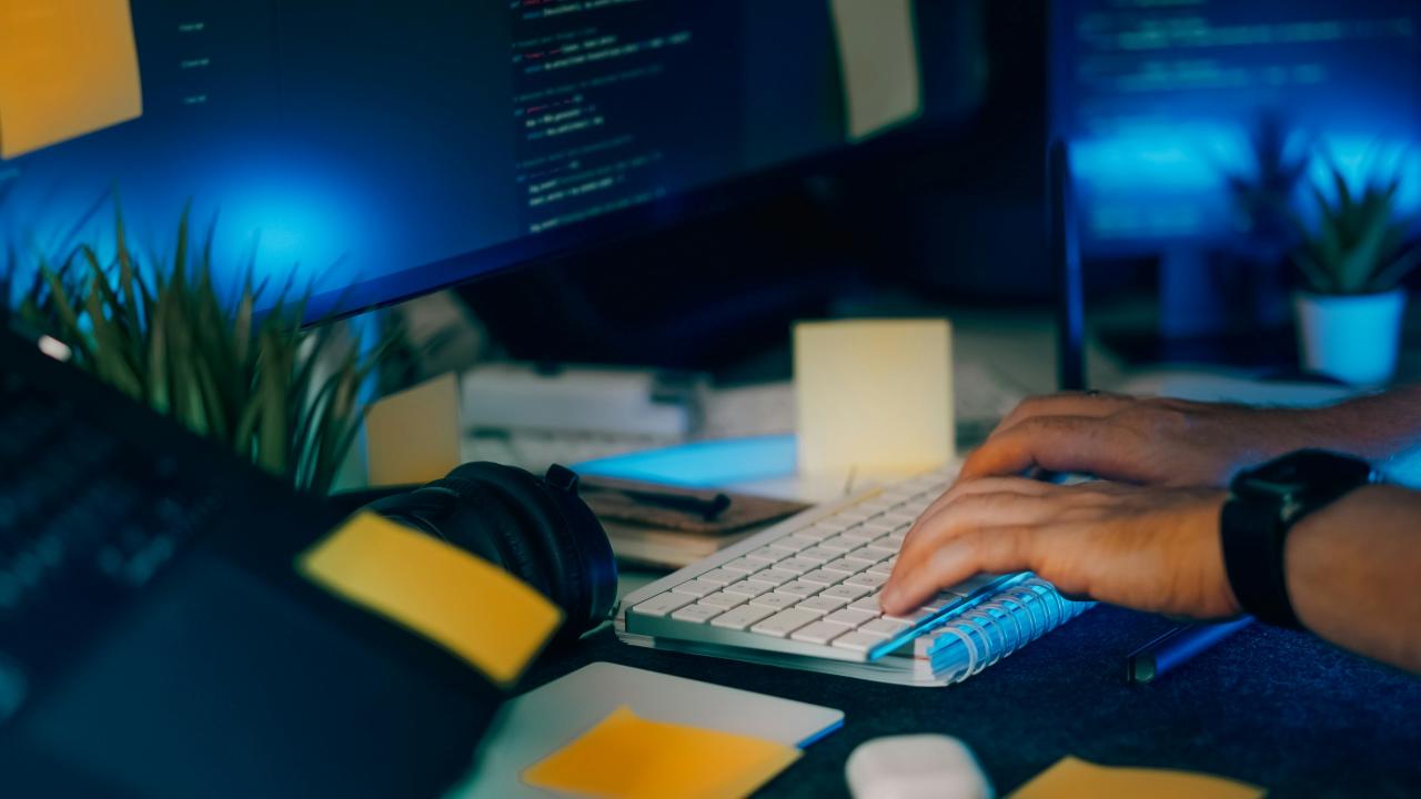 Hands typing on a keyboard with computer screens