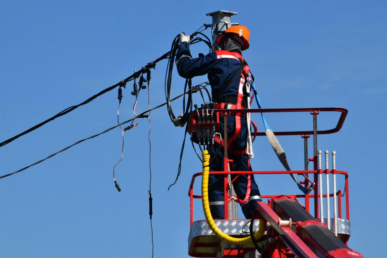 A utility worker in a hard hat and harness repairing overhead power lines